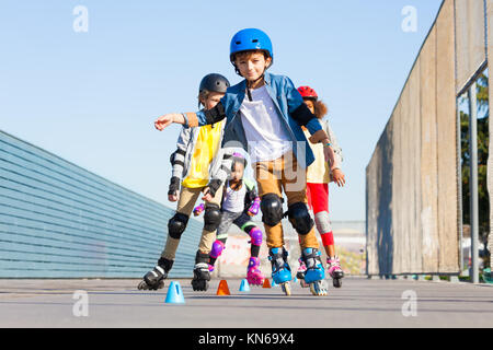 Grande gruppo di preteen ragazzi e ragazze felici inline skater, imparare a evitare i coni in corso di slalom all'aperto Foto Stock