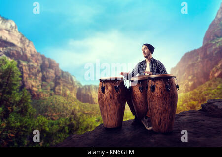 Giovane maschio batterista di bongo in legno Tamburi svolge nella vallata desertica, musicista in movimento. Djembe, musicale strumento a percussione, musica etnica Foto Stock