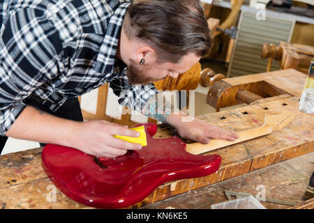 Close-up di artigiano levigazione di un collo per chitarra in legno in officina Foto Stock