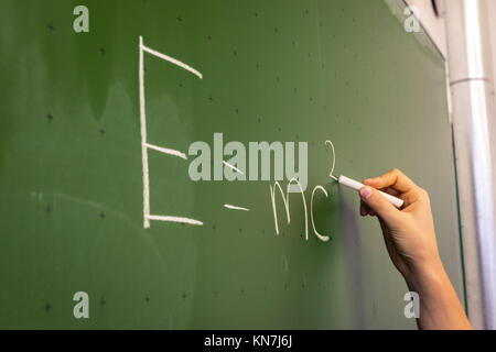 Femmina insegnante a mano scrivere sulla lavagna verde Professore Università bianco gesso collegio di istruzione lezione e = mc2 Foto Stock