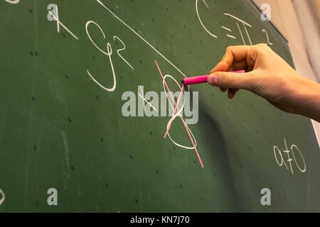 Femmina insegnante a mano scrivere sulla lavagna verde Professore Università bianco gesso collegio di istruzione matematica Lezione Numero sbagliato Foto Stock