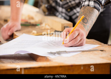 Close-up di falegname di piani e progetti scrive a disegni in officina Foto Stock