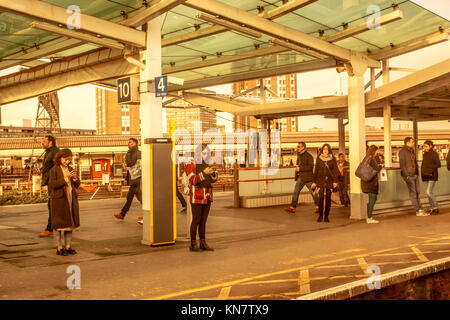 Passeggeri o persone in piedi sulla Clapham Junction banchina della stazione sud di Londra utilizzando i telefoni cellulari Foto Stock