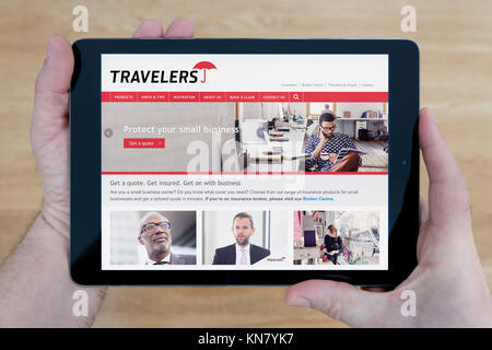 Un uomo guarda i viaggiatori sito sul suo iPad dispositivo tablet, sparato contro un tavolo di legno top sfondo (solo uso editoriale) Foto Stock