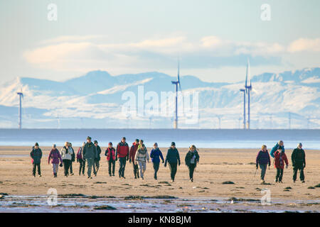 Southport, Merseyside. 11 dicembre 2017. Regno Unito Meteo. Il sole a Southport. Un gruppo di escursionisti che brave le gelide temperature per andare a fare una passeggiata sulla congelati sabbie della spiaggia di Southport nel Merseyside. Un cielo terso ha creato alcune stupende viste attraverso la coperta di neve il Galles del nord le montagne a ovest e il Cumbria brughiere a nord. Credito: Cernan Elias/Alamy Live News Foto Stock