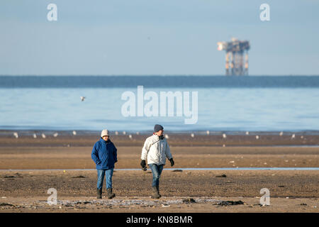 Southport, Merseyside. 11 dicembre 2017. Regno Unito Meteo. Il sole a Southport. Un gruppo di escursionisti che brave le gelide temperature per andare a fare una passeggiata sulla congelati sabbie della spiaggia di Southport nel Merseyside. Un cielo terso ha creato alcune stupende viste attraverso la coperta di neve il Galles del nord le montagne a ovest e il Cumbria brughiere a nord. Credito: Cernan Elias/Alamy Live News Foto Stock