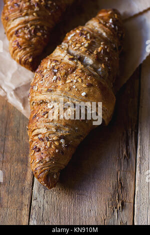 Home freschi cotti al forno di segale integrale croissant con semi di sesamo sulla carta Craft Weathered tavola di legno morbido naturale leggera colazione pasticceria francese spazio di copia Foto Stock