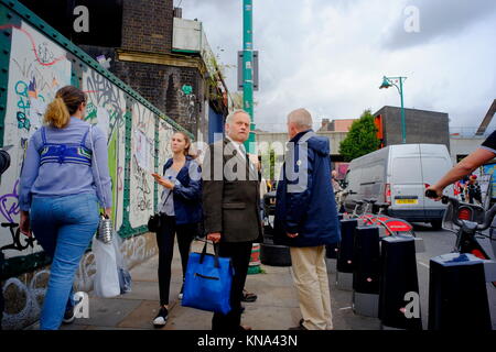 Due pensionati uomini caucasici stand di parlarsi come le donne a piedi passato su Brick Lane in Shoreditch, London, England, Regno Unito Foto Stock