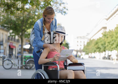 Due amici in visita città straniera una sola seduta in carrozzella Foto Stock