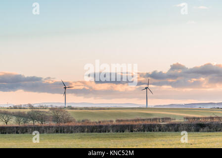 Due turbine eoliche in una fredda giornata scozzese in autunno con campi verdi e siepi e un cielo nuvoloso appena prima del tramonto. Foto Stock