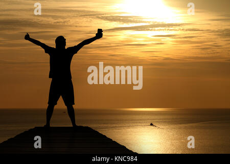 Silhouette di uomo alzando le mani al tramonto Foto Stock