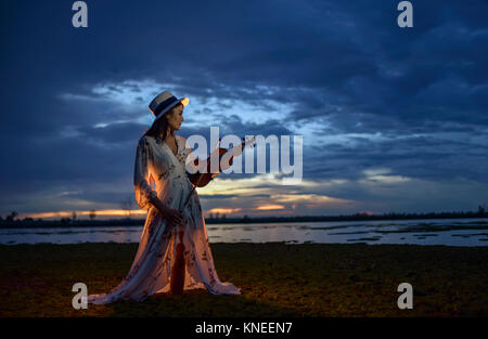 Donna in piedi sulla spiaggia al tramonto a suonare il violino Foto Stock