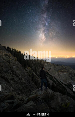 Uomo in piedi su Baldy Mountain guardando le stelle con Fresno in lontananza, California, Stati Uniti Foto Stock