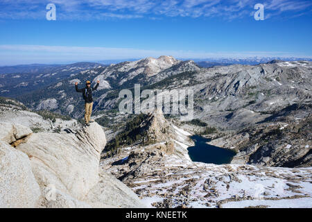 Uomo in piedi su alta Peak con le armi sollevate, lago Pear e foresta di sequoie giganti in lontananza, California, Stati Uniti Foto Stock