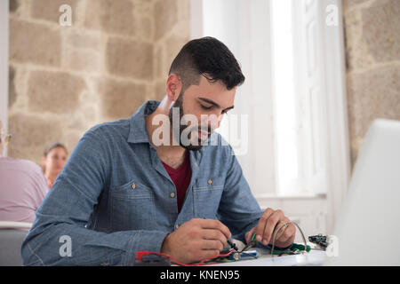 Giovane maschio tecnico informatico riparazione cavo sulla scrivania in ufficio Foto Stock