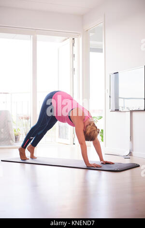 Incinta donna giovane la piegatura in avanti facendo esercizi yoga in salotto Foto Stock