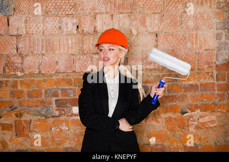 Ritratto di architetto studente o un pittore con rullo di vernice e proteggere il casco che indossa. Mattone sfondo rosso. Foto Stock