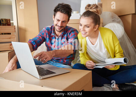 Coppia giovane a casa, circondato da scatole di cartone, guardando il computer portatile Foto Stock