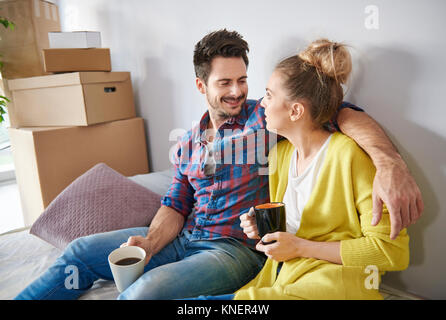 Coppia giovane a casa, circondato da scatole di cartone, bere caffè, sorridente Foto Stock