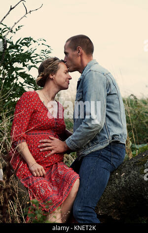 Uomo romantico kissing moglie incinta di fronte sul tronco di albero Foto Stock