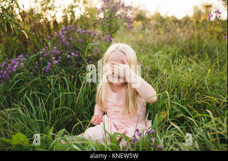 Ragazza seduta in erba alta, mano che copre gli occhi Foto Stock