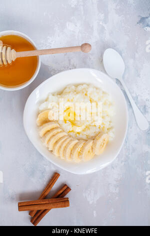 Farinata di Riso con burro, miele, banana e cannella. Vista superiore, concreto sfondo. Colazione sana nozione di porridge. Foto Stock