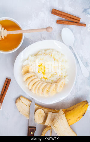 Farinata di Riso con burro, miele, banana e cannella. Vista superiore, concreto sfondo. Colazione sana nozione di porridge. Foto Stock