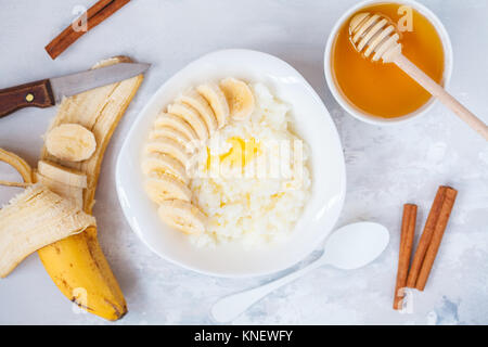 Farinata di Riso con burro, miele, banana e cannella. Vista superiore, concreto sfondo. Colazione sana nozione di porridge. Foto Stock