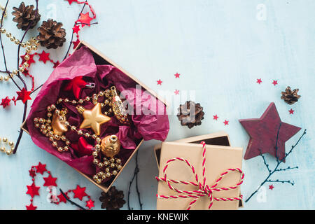 Le decorazioni di Natale in scatole artigianali con nastri, ghirlande e pigne su un bianco sullo sfondo di legno. Anno nuovo preparati. Foto Stock