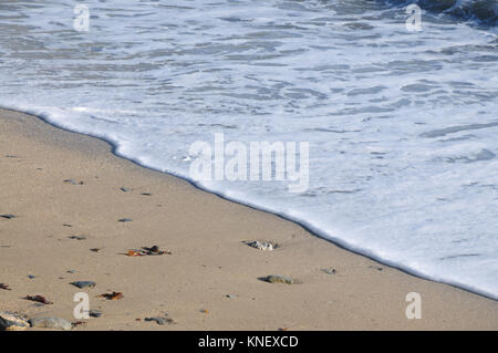 Un'onda lava fino a una spiaggia di sabbia sotto il sole Foto Stock