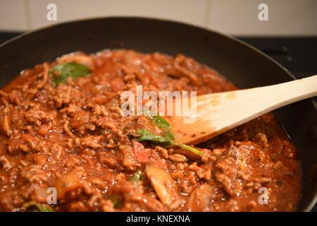 Immagine di fotografia della realizzazione di lasagne cena di famiglia con carne di agnello o di manzo cipolla funghi e salsa di pomodoro con le foglie di basilico in padella con il cucchiaio di legno Foto Stock