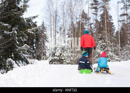 Vista posteriore dell'uomo tirando due figli sul toboga attraverso la coperta di neve forest Foto Stock