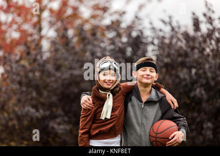 Ritratto di una ragazza e il fratello gemello che indossa il giocatore di basket e pilota i costumi di halloween in posizione di parcheggio Foto Stock