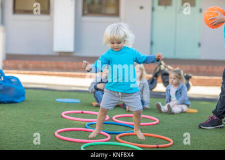 Ragazza in età prescolare, saltando al di sopra di reggette in plastica in giardino Foto Stock