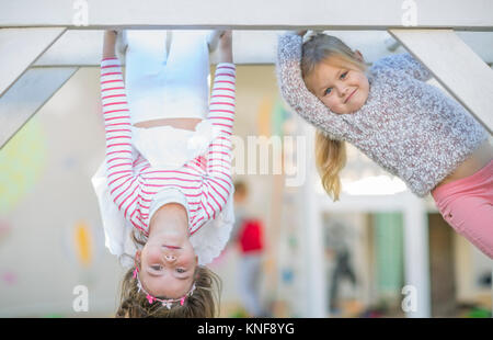 Ragazze in età prescolare, ritratto di arrampicata e capovolto sul telaio di arrampicata in giardino Foto Stock