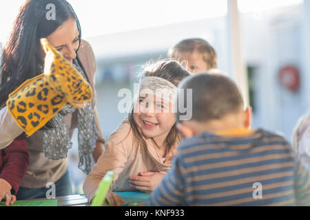 Metà donna adulta, indossando la mano marionetta, in piedi accanto a bambini, ridendo Foto Stock