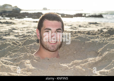 Ritratto di giovane uomo sepolto fino al suo collo nella sabbia sulla spiaggia Foto Stock