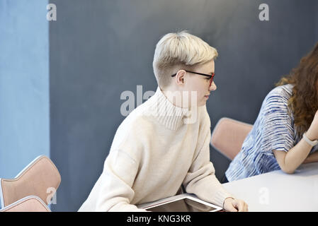 Giovane professionista imprenditrice impegnata in una discussione con i colleghi in una riunione del consiglio di amministrazione in un ufficio contemporaneo Foto Stock