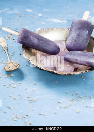Lavanda popsicles fatta di arancia congelato e il succo di limone e lo sciroppo con ciotola in argento su sfondo blu Foto Stock