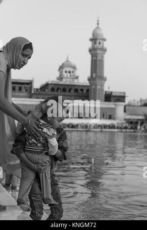 AMRITSAR, India - 20 Marzo 2016: foto in bianco e nero della famiglia indiana prima di scendere in acqua a Sri Harmandir Sahib, noto come tempio d'oro, sit Foto Stock