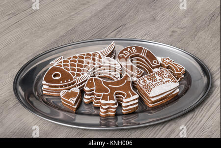 Gingerbreads natale di varie forme su una tavola di legno. Decorate a mano i cookie su un piatto d'argento con la riflessione di una pila di pasticceria. Foto Stock