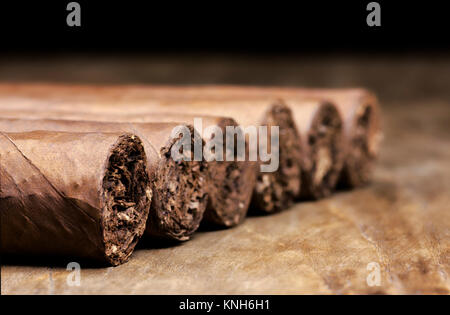 Fila di sei sigari cubani giacente su un vecchio tavolo di legno con uno sfondo sfocato Foto Stock