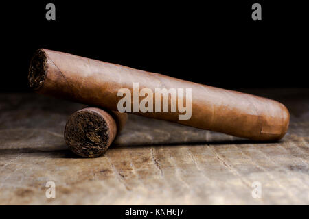 Due sigari cubani giacente su un vecchio tavolo di legno con uno sfondo sfocato Foto Stock