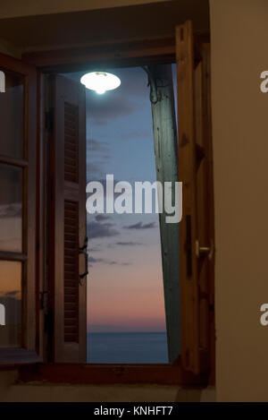 Via la luce attraverso una finestra contro un moody tramonto mediterraneo nel sud della Grecia Foto Stock