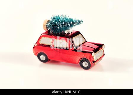Piccola e luminosa rossa auto giocattolo con albero di Natale equilibrato sul tetto per una vacanza festosa concetto su uno sfondo bianco Foto Stock