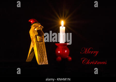 Auguri di Natale in inglese su un Norvegese Gnome Handcarved dado di legno Cracker, insieme con un lume di candela su un tipico rosso candelabro in legno. Foto Stock