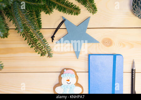 La luce di Natale in legno o il nuovo anno con sfondo verde naturale Abete rami,un notebook blu, un panpepato pupazzo di neve e di natale-tree stelle giocattolo. Foto Stock