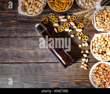 Vista superiore della birra vari snack in piastre come i pistacchi, piccolo pretzel e diverse noccioline vicino a bottiglia di birra in legno scuro, scrivania. Cibo e beverag Foto Stock