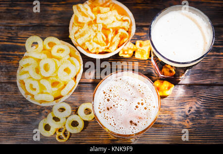 Vista dall'alto di due bicchieri di fresco con versata luce e birra scura vicino a piastre con snack e trucioli in legno scuro, scrivania. Cibo e bevande concept Foto Stock