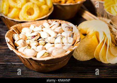 Chiusura del piatto in legno con pistacchi vicino a piastre in legno con snack in legno scuro, scrivania. Cibo e bevande concept Foto Stock